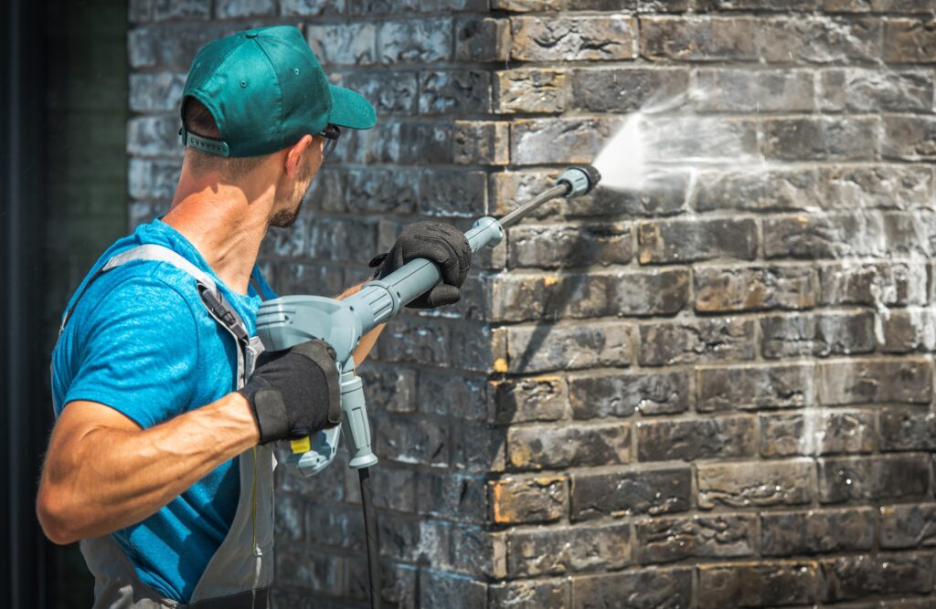 house brick wall washing using pressure washer. caucasian worker